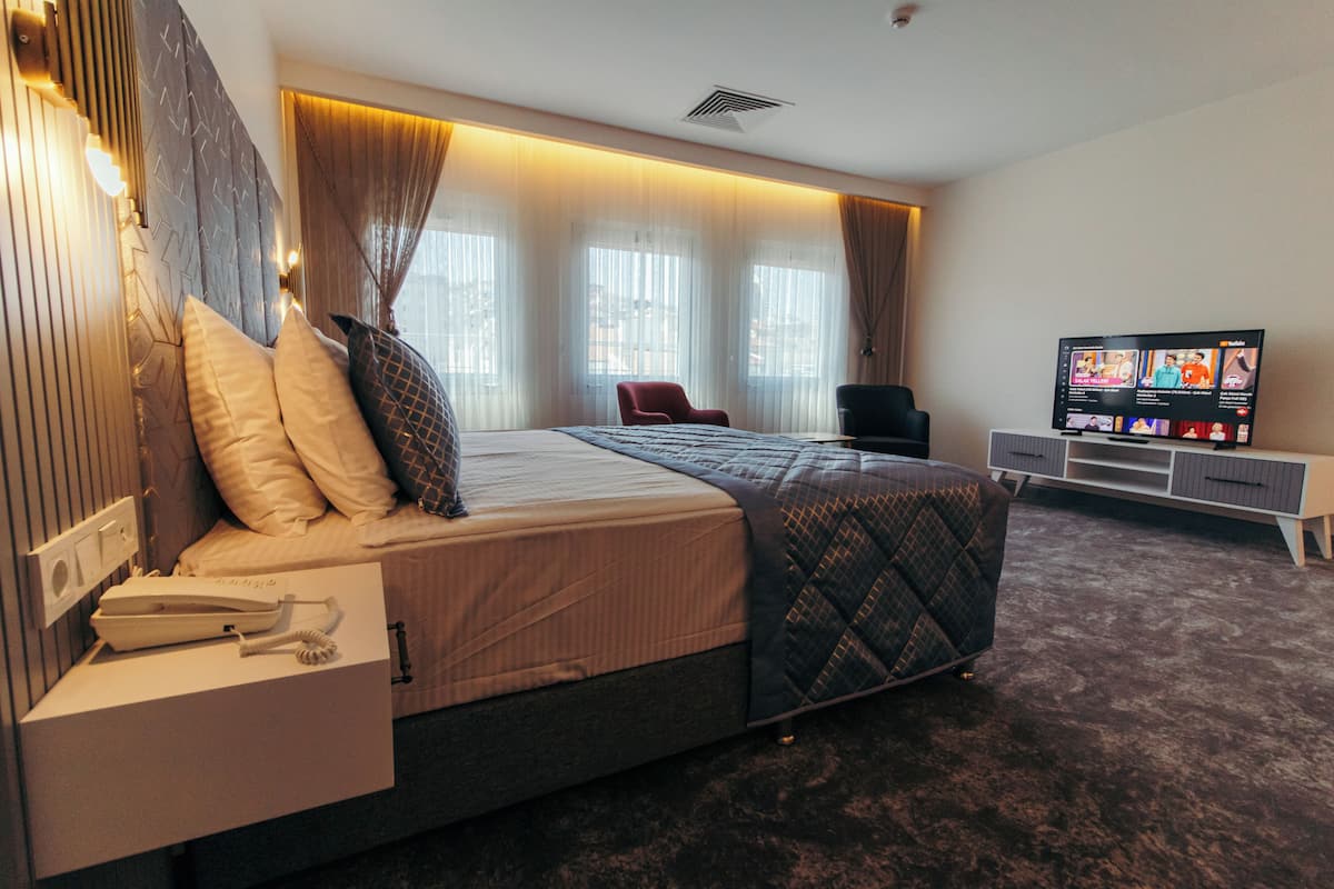 A modern hotel room with a large bed, a TV, a desk with a phone, and a red chair.