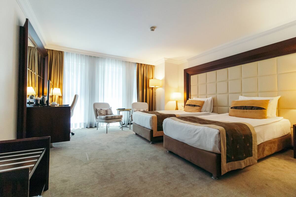 A hotel room with two beds, a desk, a chair, and a small table.