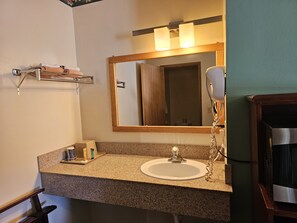 Un baño con encimera de granito, un lavabo blanco, un espejo con iluminación, un perchero y un secador de pelo.