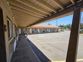 Un motel con estacionamiento techado y una fila de habitaciones con entradas individuales.