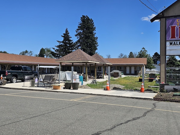 A building with a covered outdoor seating area, a parking lot, and a sign indicating a location.