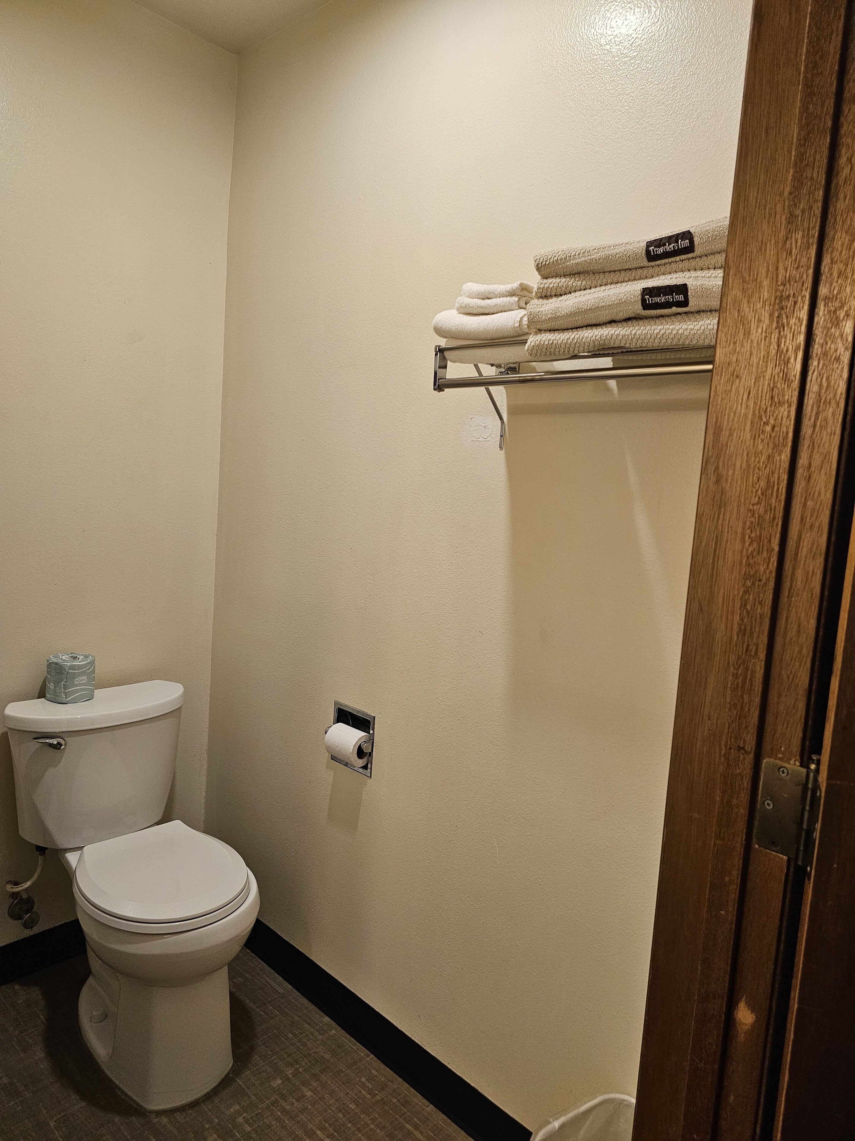 A small bathroom with a toilet, a towel rack with folded towels, and a toilet paper holder.