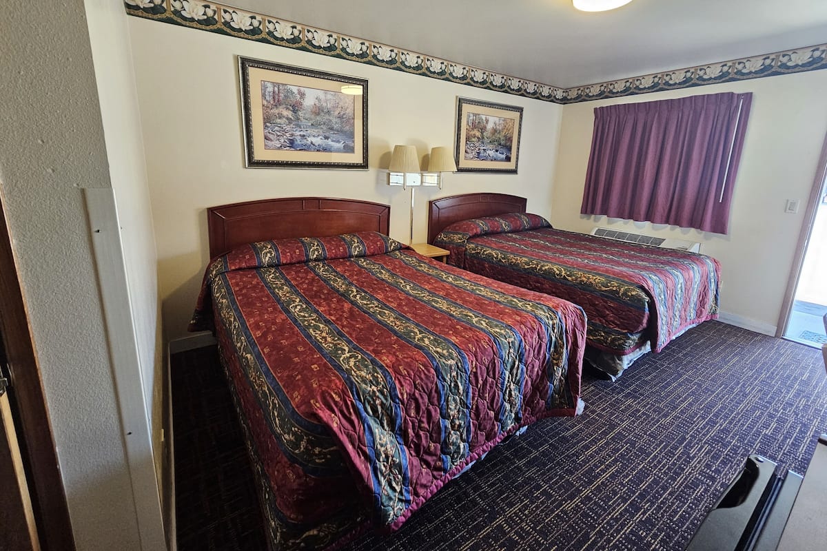 A room with two beds, a window with purple curtains, and two framed pictures on the wall.