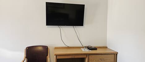 A hotel room with a wooden desk, a leather chair, a bed with a floral bedspread, and a mounted television.