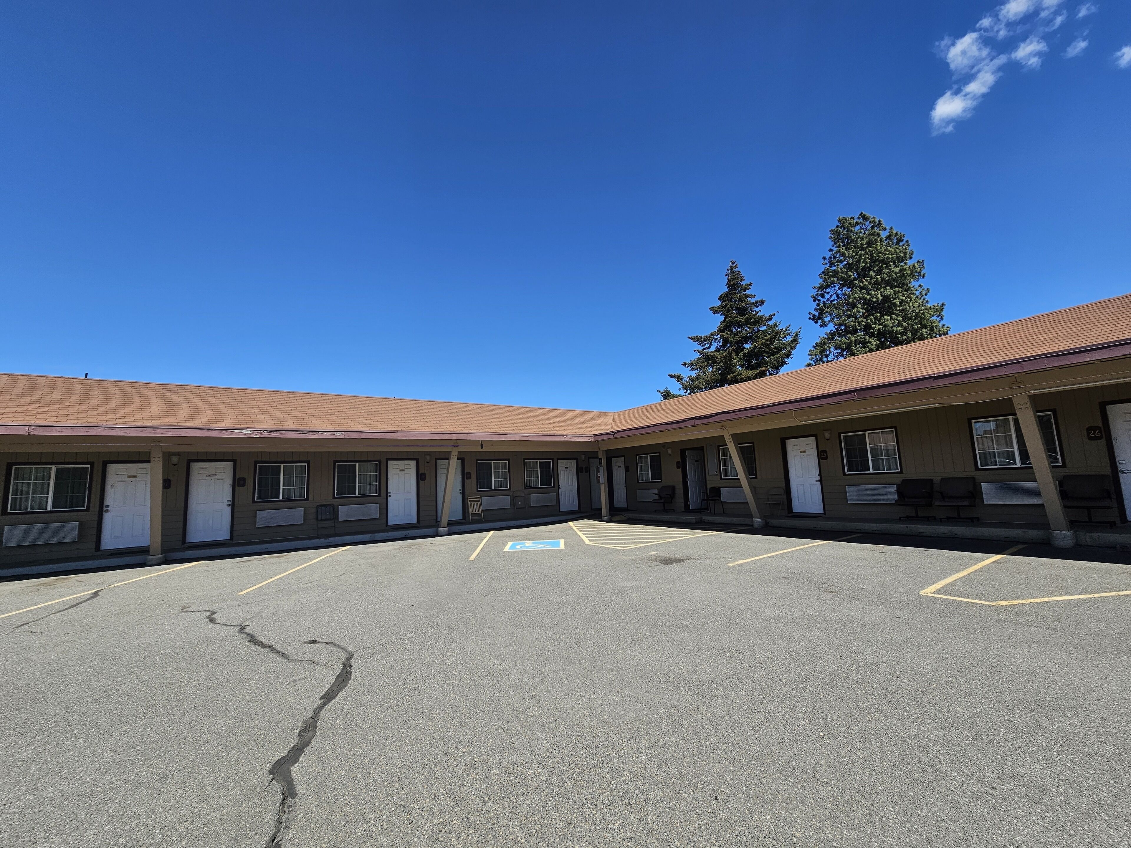 Un motel con estacionamiento, varias habitaciones y un cielo azul despejado.