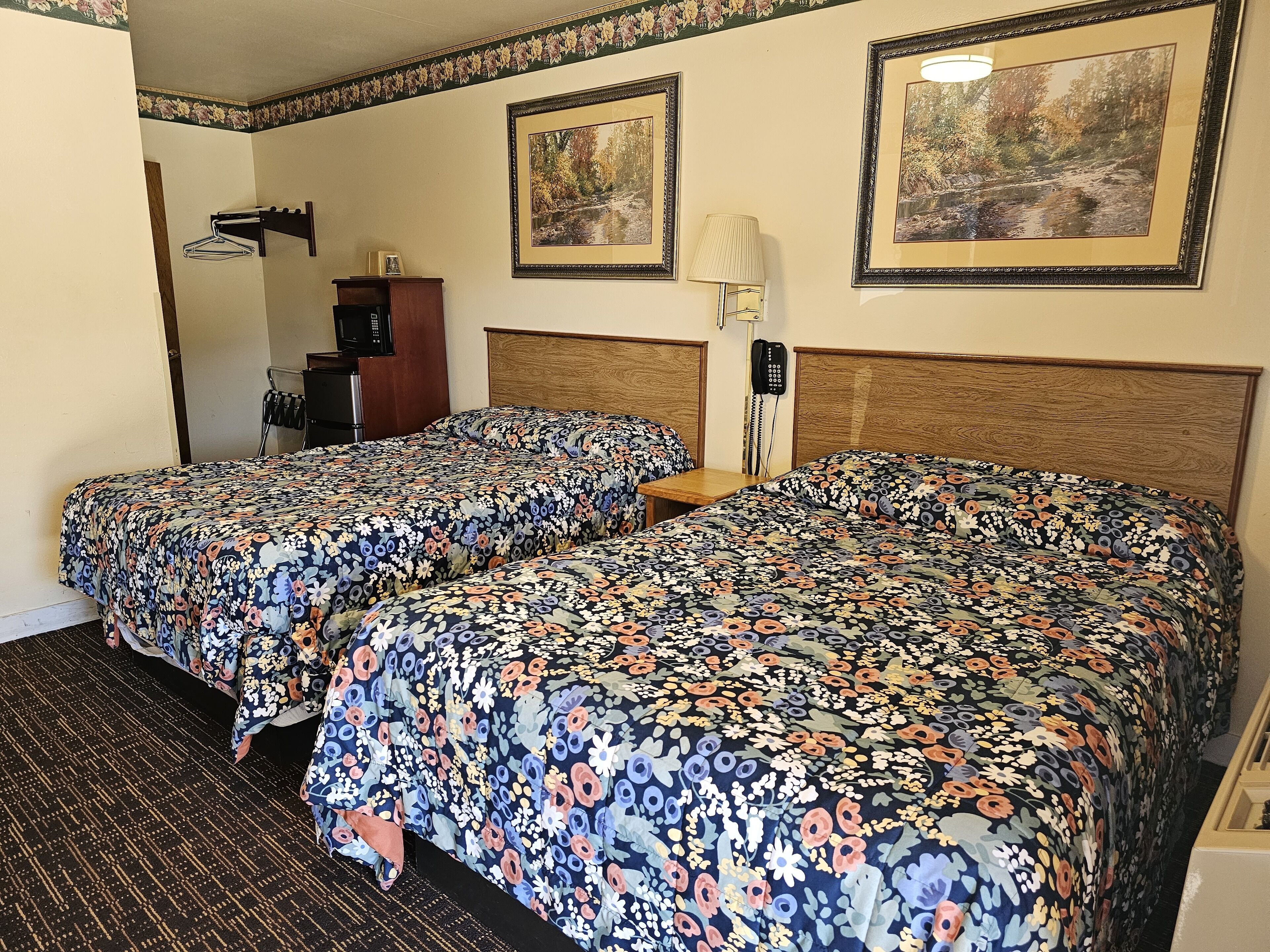 Een hotelkamer met twee bedden, een houten hoofdbord, een bureau, een lamp en twee ingelijste foto's aan de muur.