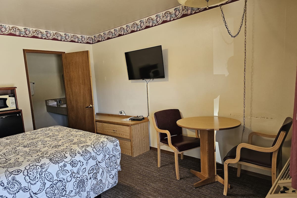 A hotel room with a bed, a desk, a chair, a television, and a small table.