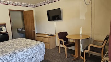 Una habitación de hotel con cama, escritorio, silla, televisor y una mesita.