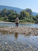 Un hombre de pie en la orilla rocosa de un río, con un promontorio boscoso al fondo.
