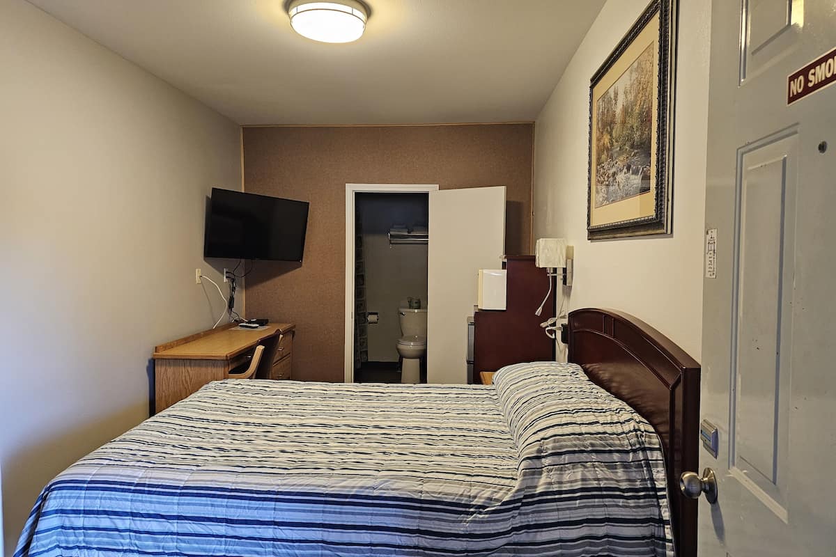 A hotel room with a bed, a desk, a TV, a door, and a painting on the wall.