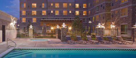 Un hotel con piscina, sillones de descanso y fachada de piedra.