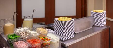 Un buffet allestito con diversi contenitori per alimenti e una pila di piatti.