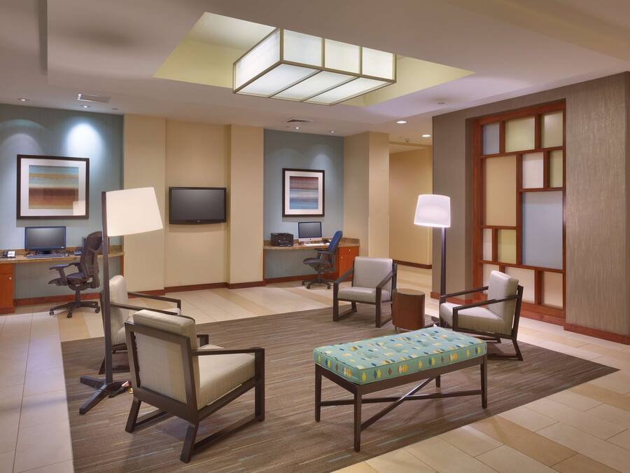 Um hall de hotel com uma mesa de recepção, várias áreas de estar, uma televisão de tela plana e obras de arte nas paredes.