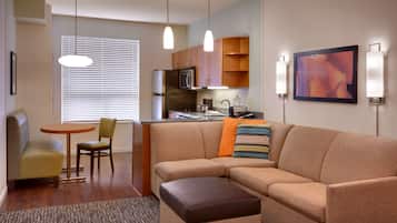 A modern living room with a sofa, ottoman, and a dining area with a table and chairs.