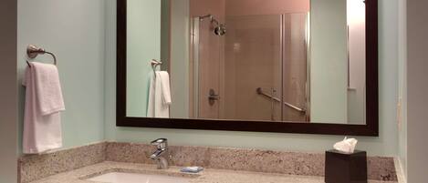 A bathroom with a large mirror, a sink, a towel rack, and a shelf with towels and a hairdryer.