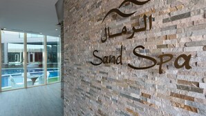 Un letrero de spa con texto en árabe y 'Sand Spa' en inglés, sobre un muro de piedra.