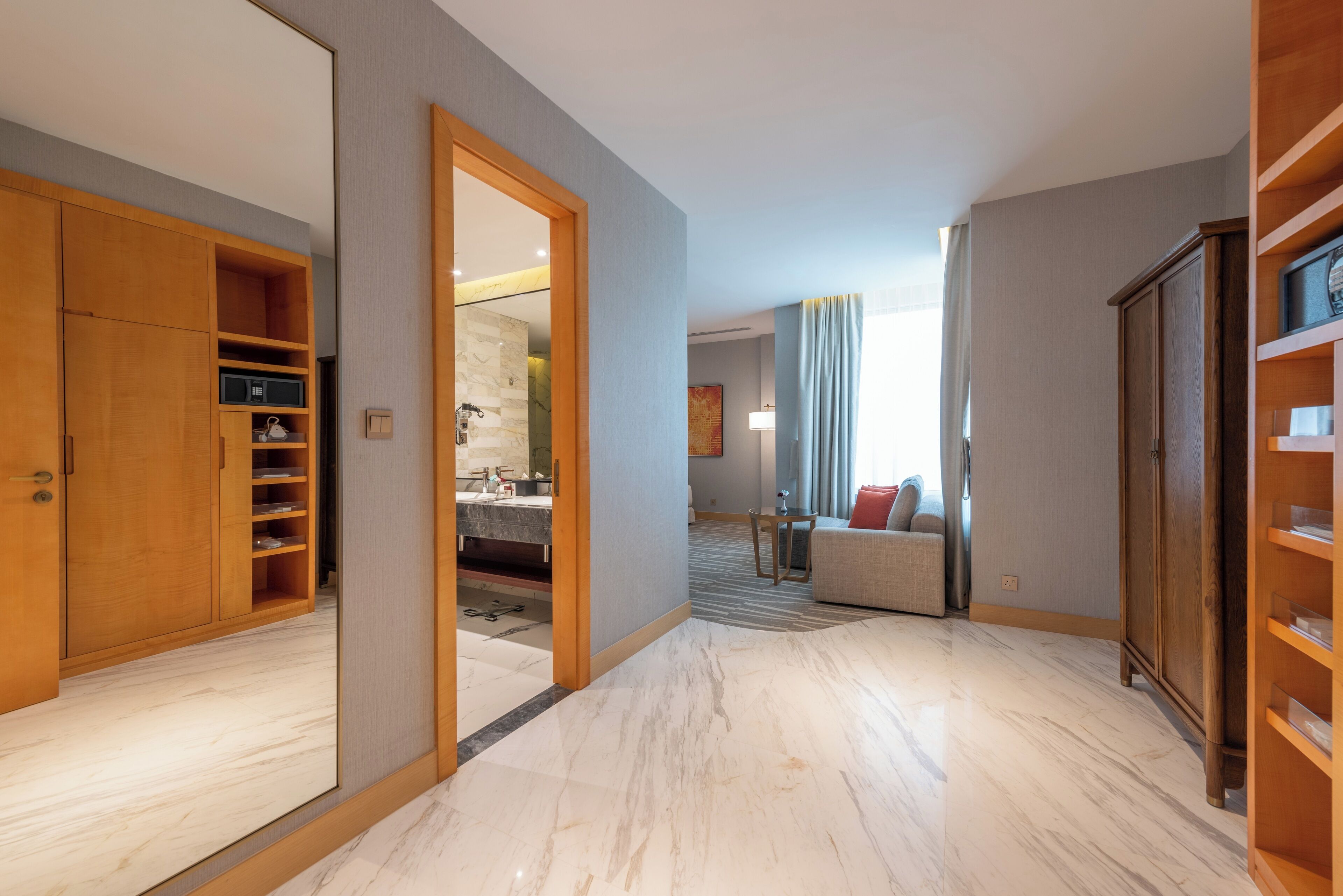A spacious hallway with a wooden wardrobe, a bathroom with a marble floor, and a seating area with a sofa and curtains.