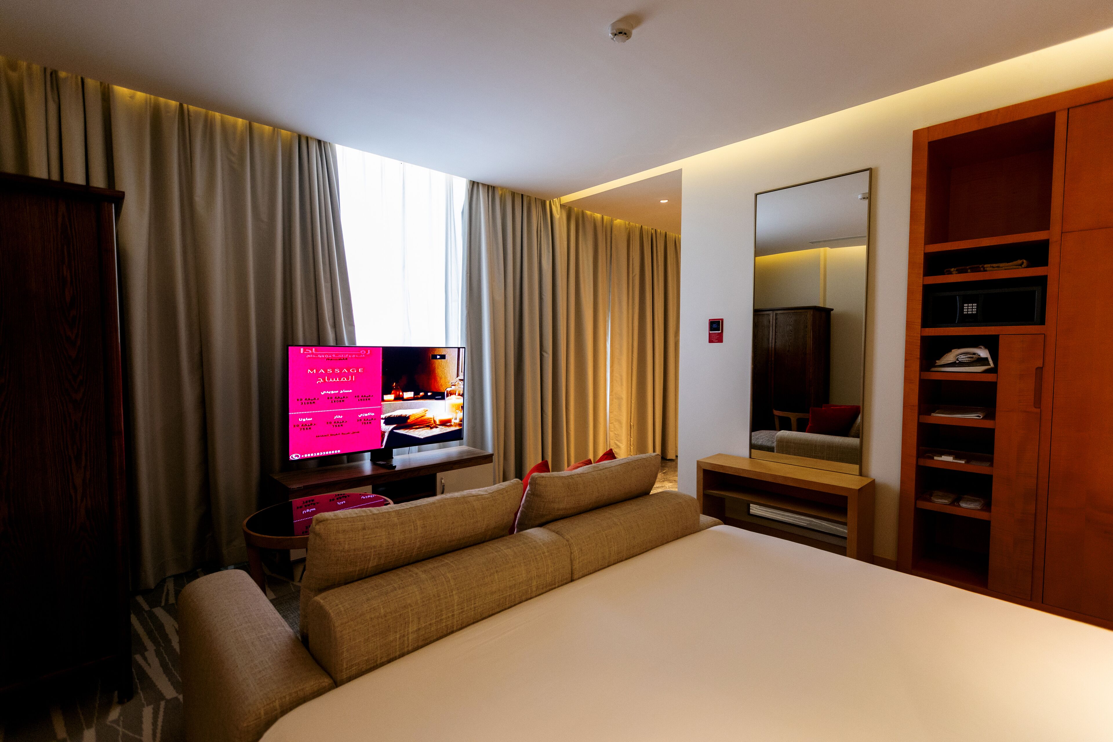 Ein Hotelzimmer mit einem Bett, einem Fernseher, einem Schreibtisch, einem Spiegel und einem Kleiderschrank.