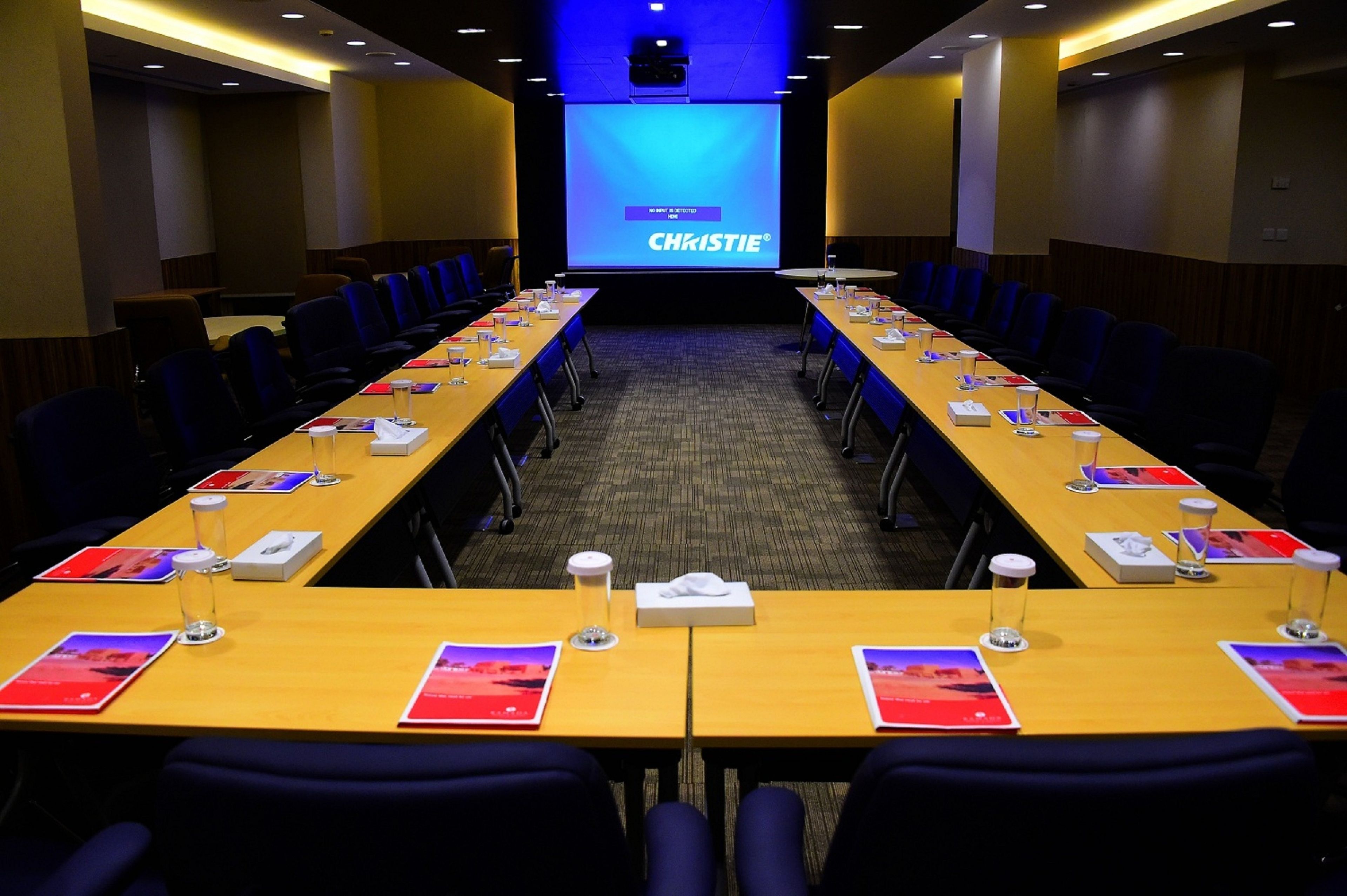 A conference room with a long table, chairs, and a presentation screen.