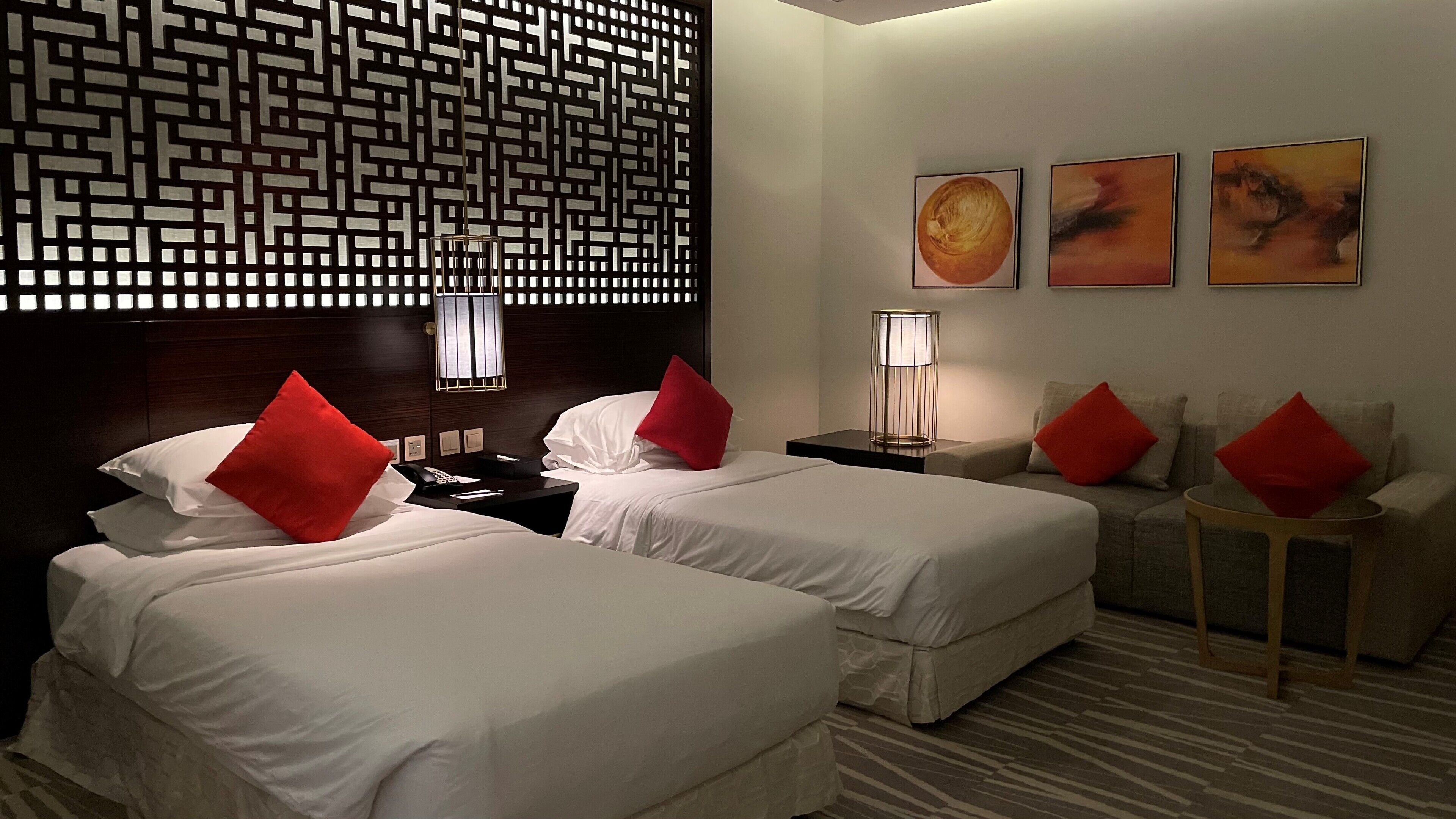 Habitación de hotel con dos camas, un sofá y un panel decorativo en la pared.