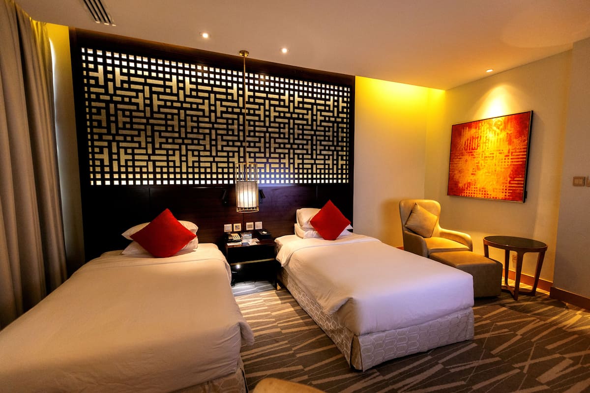Ein Hotelzimmer mit zwei Betten, einem Nachttisch, einem Sessel, einem kleinen Tisch und einer dekorativen Wandverkleidung.