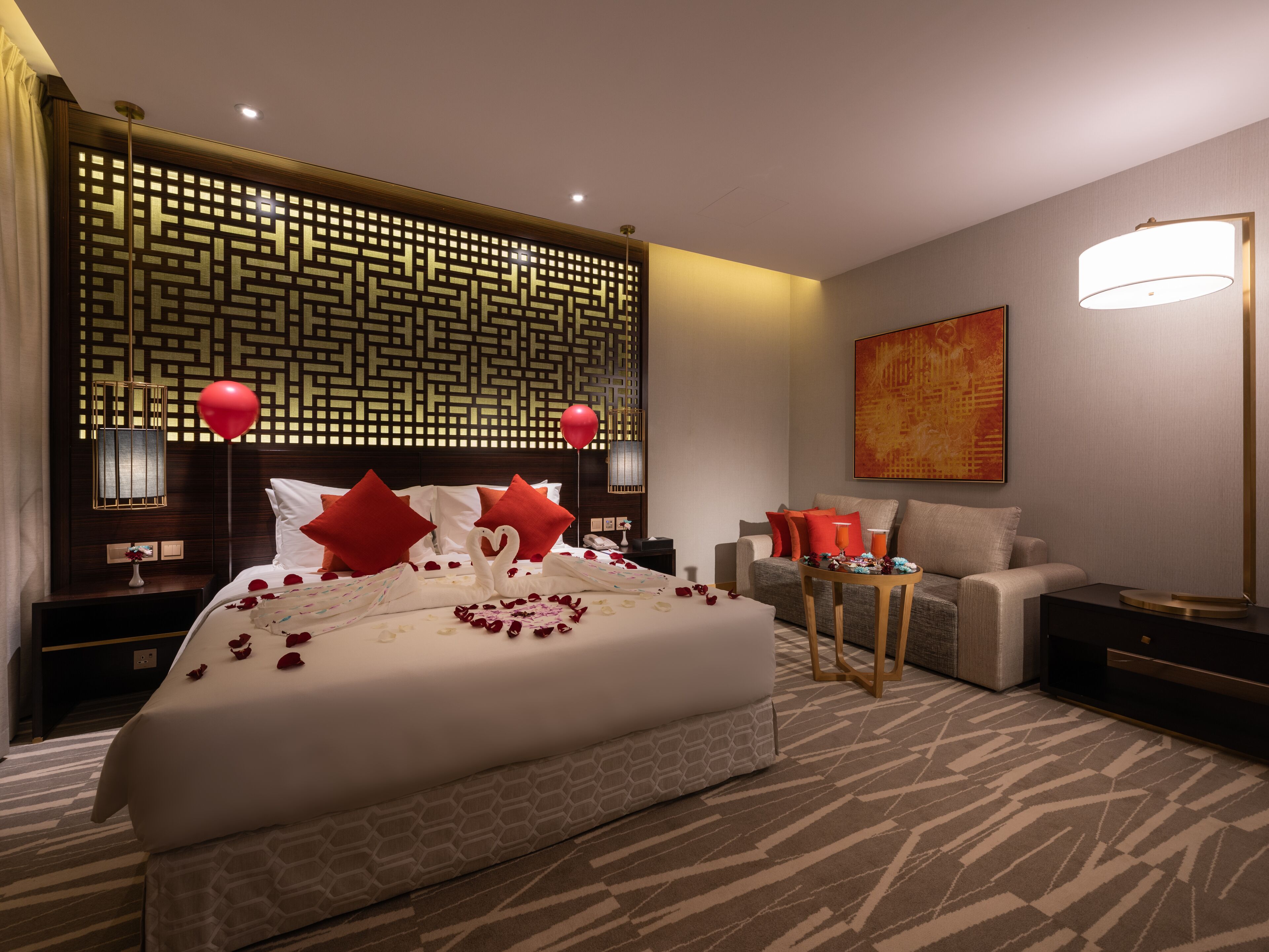 Una habitación de hotel moderna con una cama grande, un cabecero decorativo, un sofá, una mesita y una obra de arte colgada en la pared.