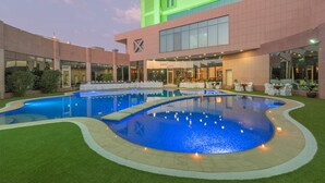 Un hotel con una amplia piscina exterior, un área de estar techada y una fachada de edificio moderna.