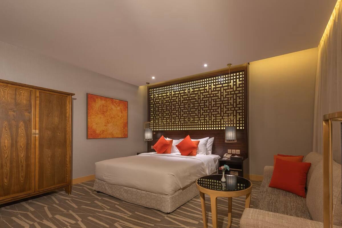 Ein Hotelzimmer mit einem großen Bett, einem Holzschrank, einer dekorativen Wandverkleidung, einem kleinen runden Tisch und einer Couch mit Kissen.