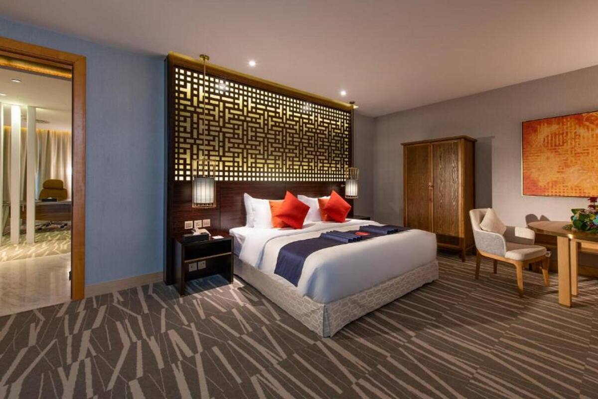 Ein Hotelzimmer mit einem großen Bett, einem Nachttisch, einem Schreibtisch mit Stuhl, einem Kleiderschrank und einer Zierverkleidung an der Wand.