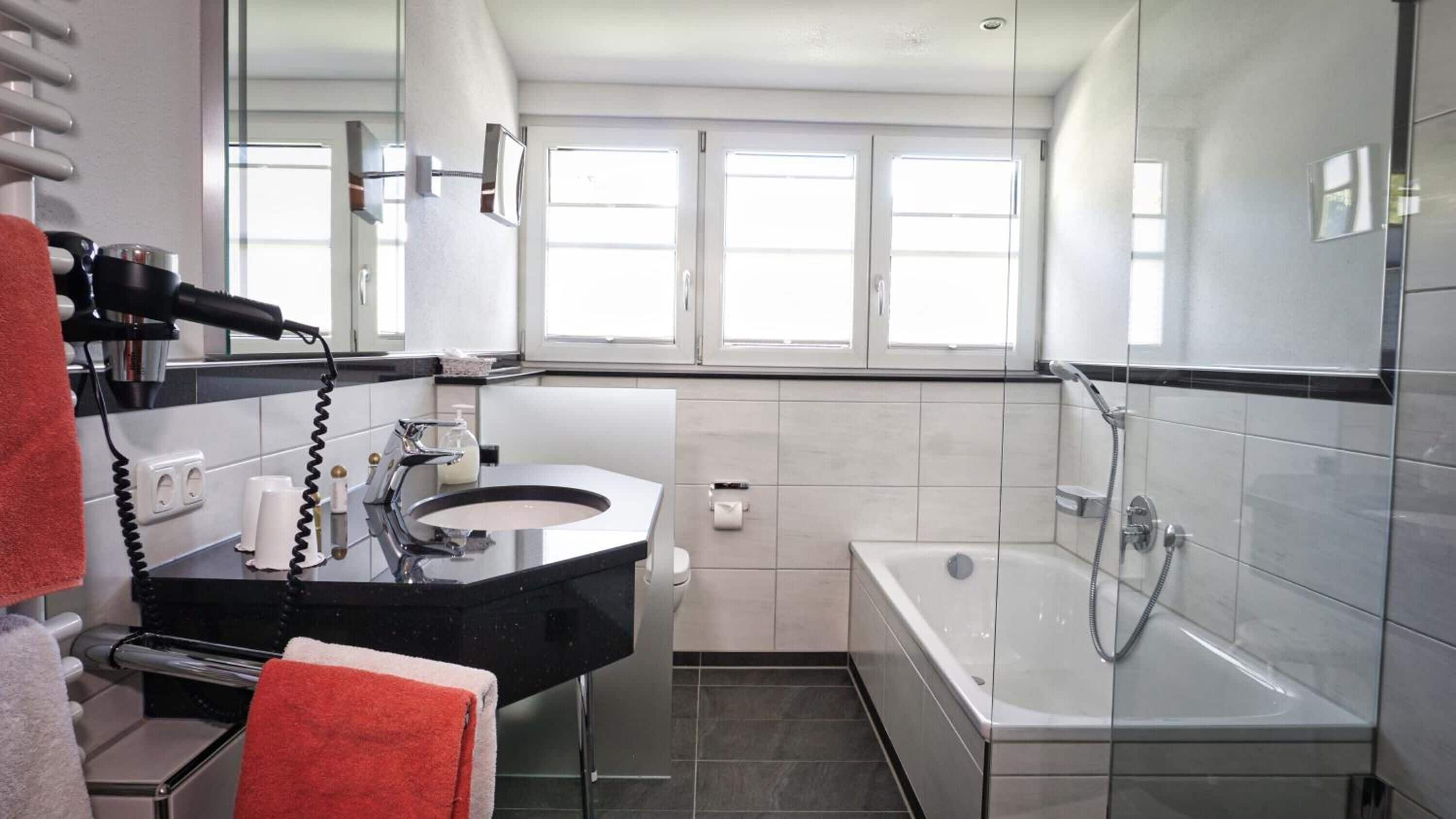 Une salle de bain moderne avec un meuble-lavabo noir, une douche à parois de verre et une grande fenêtre qui laisse entrer la lumière naturelle.