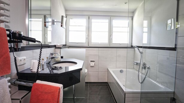 Un baño moderno con tocador negro, ducha con cerramiento de vidrio y un ventanal que proporciona luz natural.
