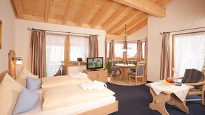 Una habitación acogedora con techo de madera, un sofá con almohadones, televisor, mesa de comedor con sillas y una ventana con cortinas.