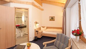 Habitación de hotel pequeña con una cama individual, una mesita de noche, una silla, una ventana con cortinas y vistas al exterior.