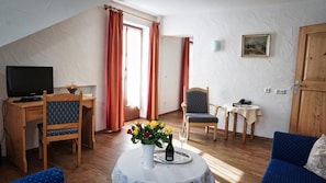 Une pièce chaleureuse avec un bureau en bois, une télévision, un fauteuil confortable, une petite table ornée d’un vase de fleurs et un canapé bleu.