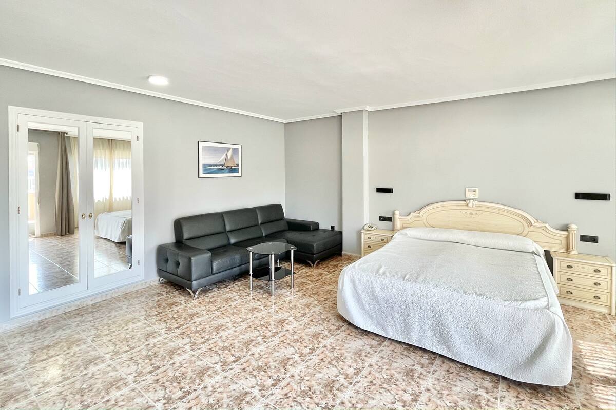 A bedroom with a bed, a sofa, a nightstand, a mirror, and a door leading to a balcony.