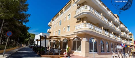 A multi-story hotel with balconies, outdoor seating, and a clear blue sky.