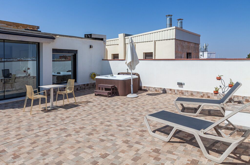 Una terrazza sul tetto con una vasca idromassaggio, poltrone relax e un tavolo con sedie.