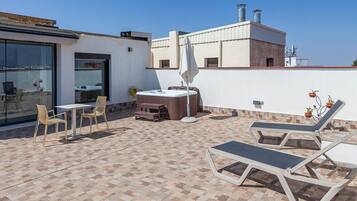 Una terrazza sul tetto con una vasca idromassaggio, poltrone relax e un tavolo con sedie.