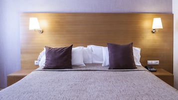 A neatly made bed with a wooden headboard, two bedside lamps, and a remote control on the nightstand.