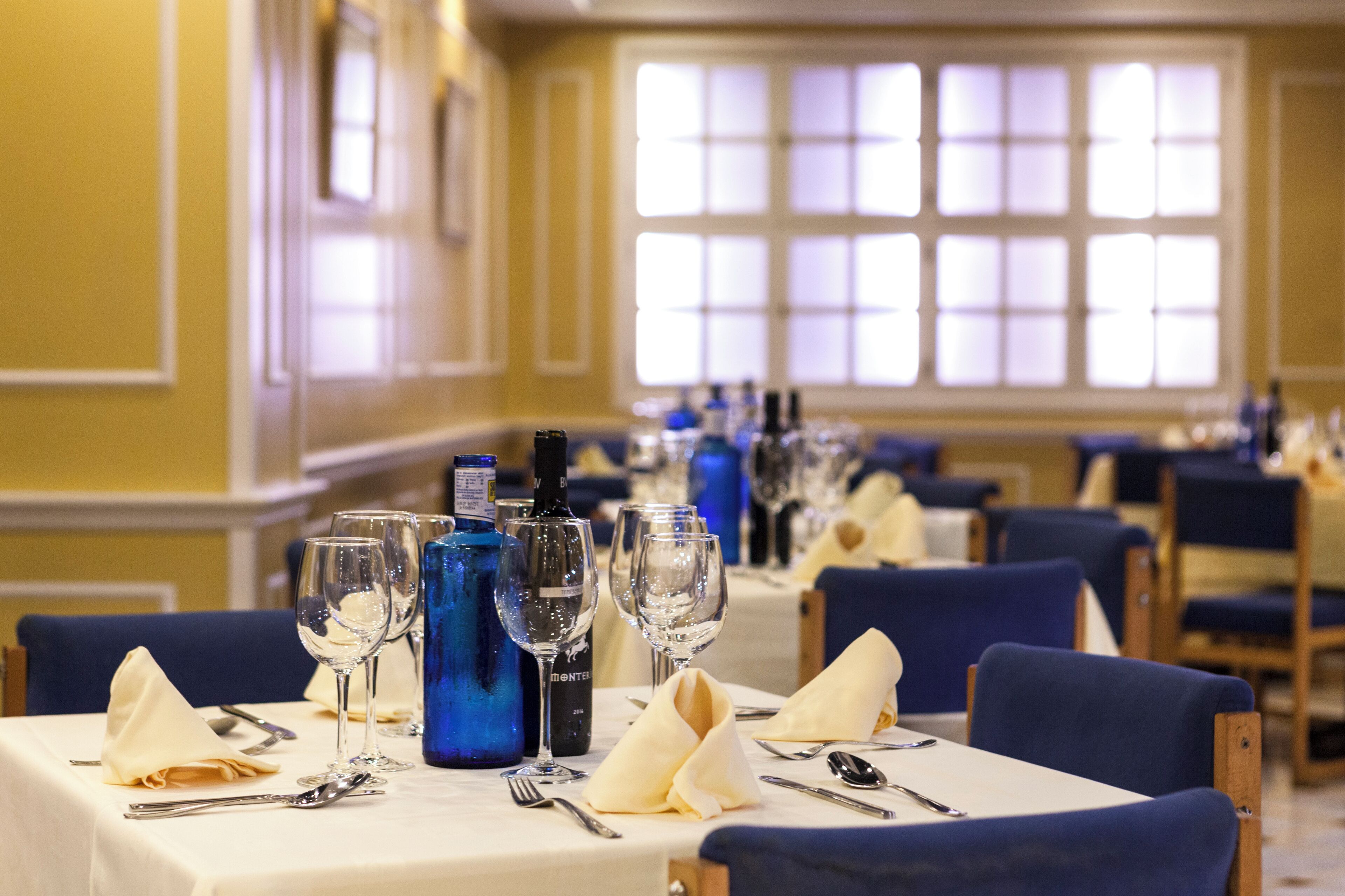 A dining area with tables set for service, featuring blue glassware and a bottle of wine.