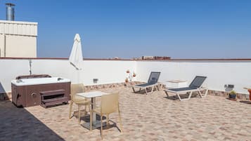 Una terraza en la azotea con jacuzzi, sillones de descanso y una mesa.