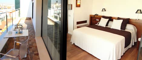 A hotel room with a balcony, a bed with multiple pillows, a bedside table, and a lamp.