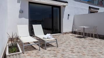 Un área de estar moderna al aire libre con puerta de cristal que da a una piscina, sillones blancos y suelo de baldosas.