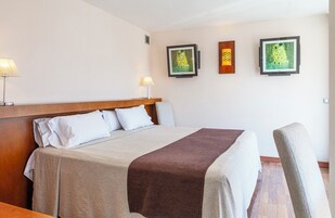 Une chambre d’hôtel avec un lit, deux lampes de chevet et trois œuvres d’art encadrées accrochées au mur.