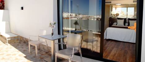 Una habitación de hotel moderna con balcón, un área de comedor con mesa y sillas, y una cama con vistas.