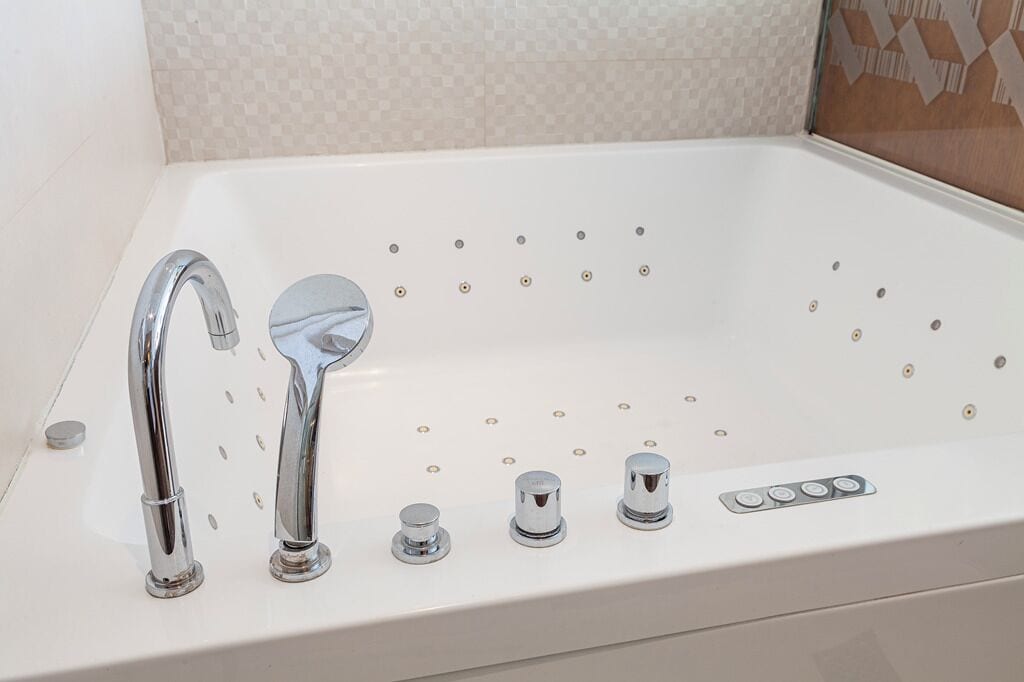 A white bathtub with a single chrome faucet and three control knobs.