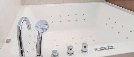 A white bathtub with a single chrome faucet and three control knobs.
