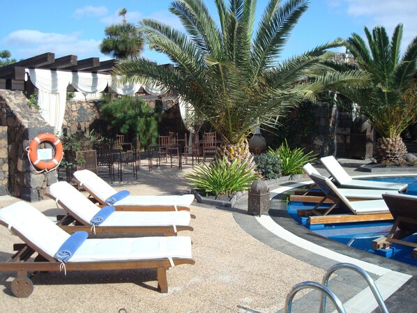 A poolside area with lounge chairs, a lifebuoy, and a stone wall with draped fabric.