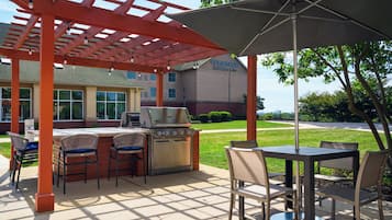 An outdoor patio with a grill, chairs, and a table under a pergola.