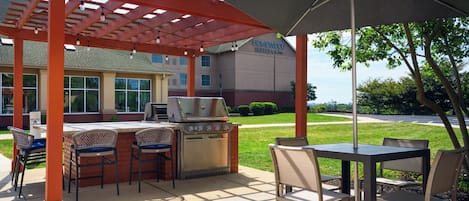 An outdoor patio with a grill, chairs, and a table under a pergola.